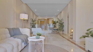 A modern living room with a sofa, a coffee table, and a dining area in the background. - Mimosas de Ban s 10 2 2 E (Marbella)