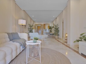 A modern living room with a sofa, a coffee table, and a dining area in the background. - Mimosas de Ban s 10 2 2 E (Marbella)