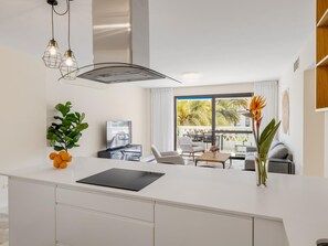 A modern kitchen with a central island, a dining area with a table and chairs, and a view of palm trees through large windows. - 2 Dormitorios Playas del Duque ref 229 (Marbella)