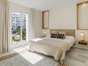 A hotel room with a large bed, a view of a building complex, and a balcony with curtains. - 2 Dormitorios Playas del Duque ref 229 (Marbella)