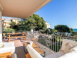 Ein Balkon mit Holztisch und -stühlen, einer Sitzecke und Blick auf das Meer und die Gebäude.