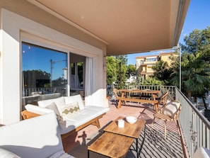 Ein Balkon mit einer Couch, einem Holztisch und Stühlen, mit Blick auf ein Wohngebiet mit Bäumen und Gebäuden.