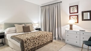 A hotel room with a bed, bedside tables, a desk, a chair, a lamp, and curtains. - Apartamento en Playas del Duque ref 102 (Marbella)