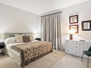 A hotel room with a bed, bedside tables, a desk, a chair, a lamp, and curtains. - Apartamento en Playas del Duque ref 102 (Marbella)