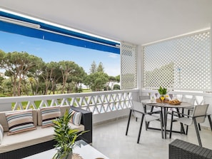 A balcony with a white lattice partition, a round table with chairs, a sofa with striped cushions, and a potted plant. - Apartamento en Playas del Duque ref 102 (Marbella)