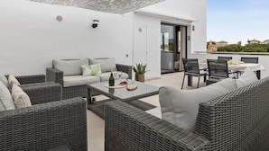 A covered outdoor seating area with wicker furniture, a table with drinks, and a view of the surrounding landscape. - Tico con Vistas al mar (Marbella)