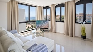 A modern living room with a sofa, a coffee table, and a painting. Large windows offer a view of the city. - Tico con Vistas al mar (Marbella)