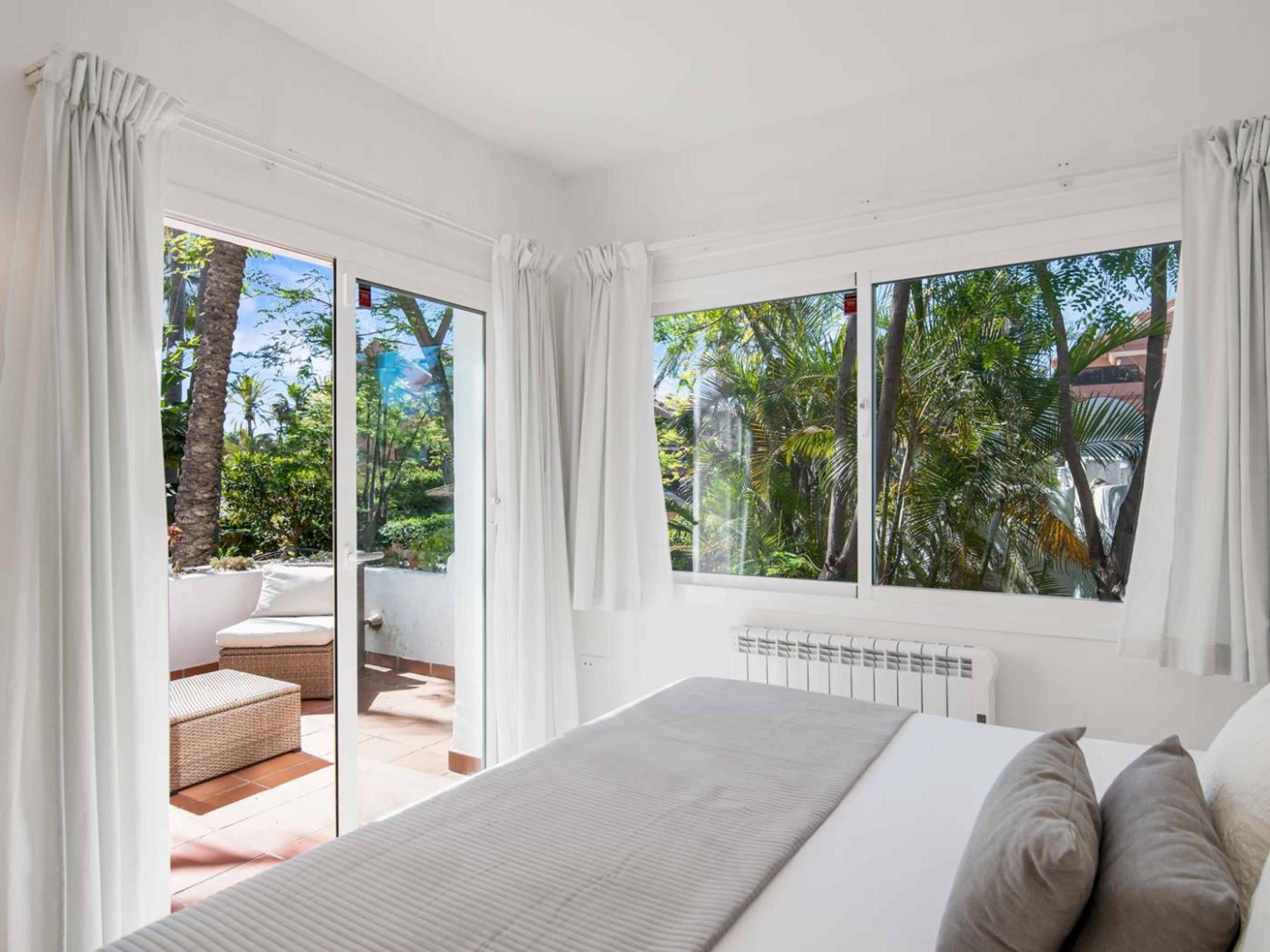 Un dormitorio con cama, radiador y vista a un jardín a través de ventanas amplias.