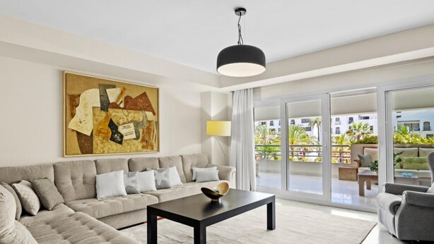 A modern living room with a sofa, a coffee table, and a large painting on the wall. - Amplio Apartamento en Playas del Duque (Marbella)