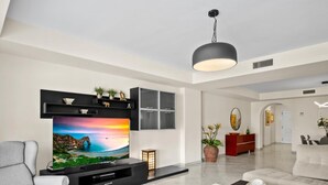 A modern living room with a flat-screen TV, a sofa, a coffee table, and a dining area. - Amplio Apartamento en Playas del Duque (Marbella)