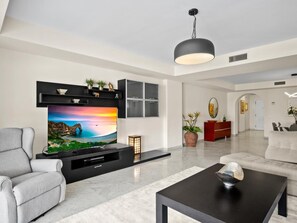 A modern living room with a flat-screen TV, a sofa, a coffee table, and a dining area. - Amplio Apartamento en Playas del Duque (Marbella)
