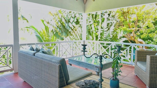 A covered outdoor seating area with wicker furniture, a decorative metal candelabra, and a potted plant.