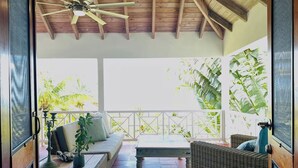 An open-air patio with wicker furniture, a ceiling fan, and a view of greenery.