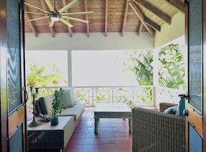 Une terrasse extérieure avec des meubles en osier, un ventilateur de plafond et une vue sur la verdure.