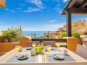 A table set with breakfast items and drinks, overlooking a coastal cityscape. - Apartamento Junto al mar en Estepona (Estepona)