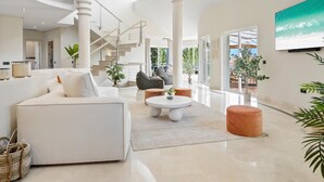 A spacious living area with a white sofa, a round coffee table, and a staircase leading to an upper floor. - Preciosa Villa con Magn Ficas Vistas en Los Flamin (Benahavis)