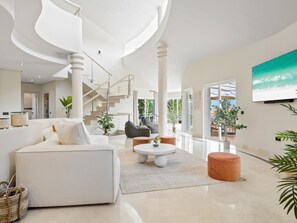 A spacious living area with a white sofa, a round coffee table, and a staircase leading to an upper floor. - Preciosa Villa con Magn Ficas Vistas en Los Flamin (Benahavis)