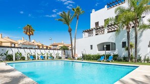 A swimming pool with lounge chairs, palm trees, and a white building with a pergola. - Privilegio Marbella (Marbella)