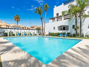 A swimming pool with lounge chairs, palm trees, and a white building with a pergola. - Privilegio Marbella (Marbella)