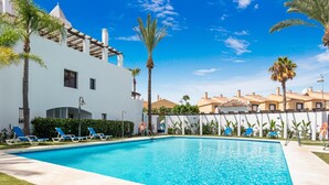 A swimming pool with lounge chairs, palm trees, and a white building with a tiled roof. - Privilegio Marbella (Marbella)