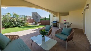 Een terras met buitenmeubilair, een barbecue en uitzicht op een tuin.
