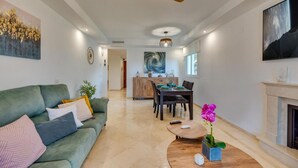 Een moderne woonkamer met een bank, salontafel en een eethoek met een tafel voor vier personen.