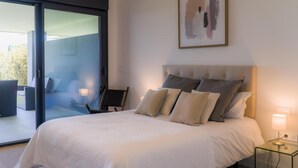 Een moderne slaapkamer met een groot bed, een glazen deur naar een buitenruimte, een nachtkastje met een lamp en een lijst met een abstract schilderij aan de muur.