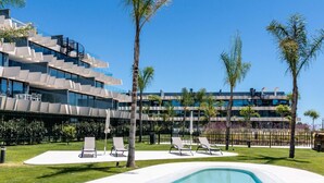Een modern hotel met een zwembad, ligbedden en palmbomen.