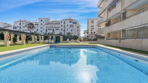 A swimming pool with a clear blue water surface, surrounded by a well-maintained lawn and a pergola structure. - Marina Ban s c Ntrico Apartamento (Marbella)