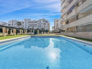 A swimming pool with a clear blue water surface, surrounded by a well-maintained lawn and a pergola structure. - Marina Ban s c Ntrico Apartamento (Marbella)