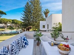 Ein Sitzbereich im Freien mit Pool, weißer Möbel und verschiedenen Pflanzen.