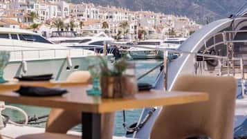 Puerto deportivo con barcos amarrados, una mesa con sillas y vistas a edificios costeros.
