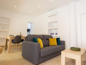 Ein modernes Wohnzimmer mit grauem Sofa, einem Holzesstisch und einem kleinen Beistelltisch.