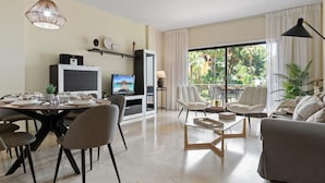 A modern living room with a dining area, a flat-screen TV, and a balcony with a view of palm trees. - Gran Terraza ref ADM 116 (Marbella)