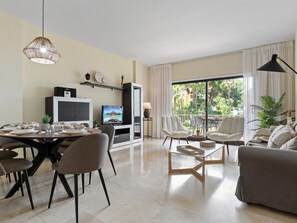 Ein modernes Wohnzimmer mit Essbereich, einem Flachbildfernseher und einem Balkon mit Blick auf Palmen.