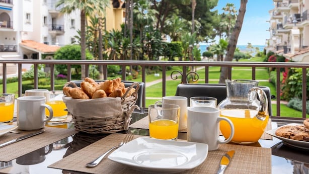 A breakfast table with croissants, orange juice, and coffee cups, overlooking a garden and buildings. - Gran Terraza ref ADM 116 (Marbella)