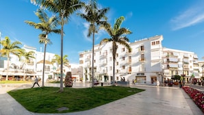 A plaza with palm trees, a café, and white buildings with balconies. - Contemporaly Huge Riyad (Estepona)