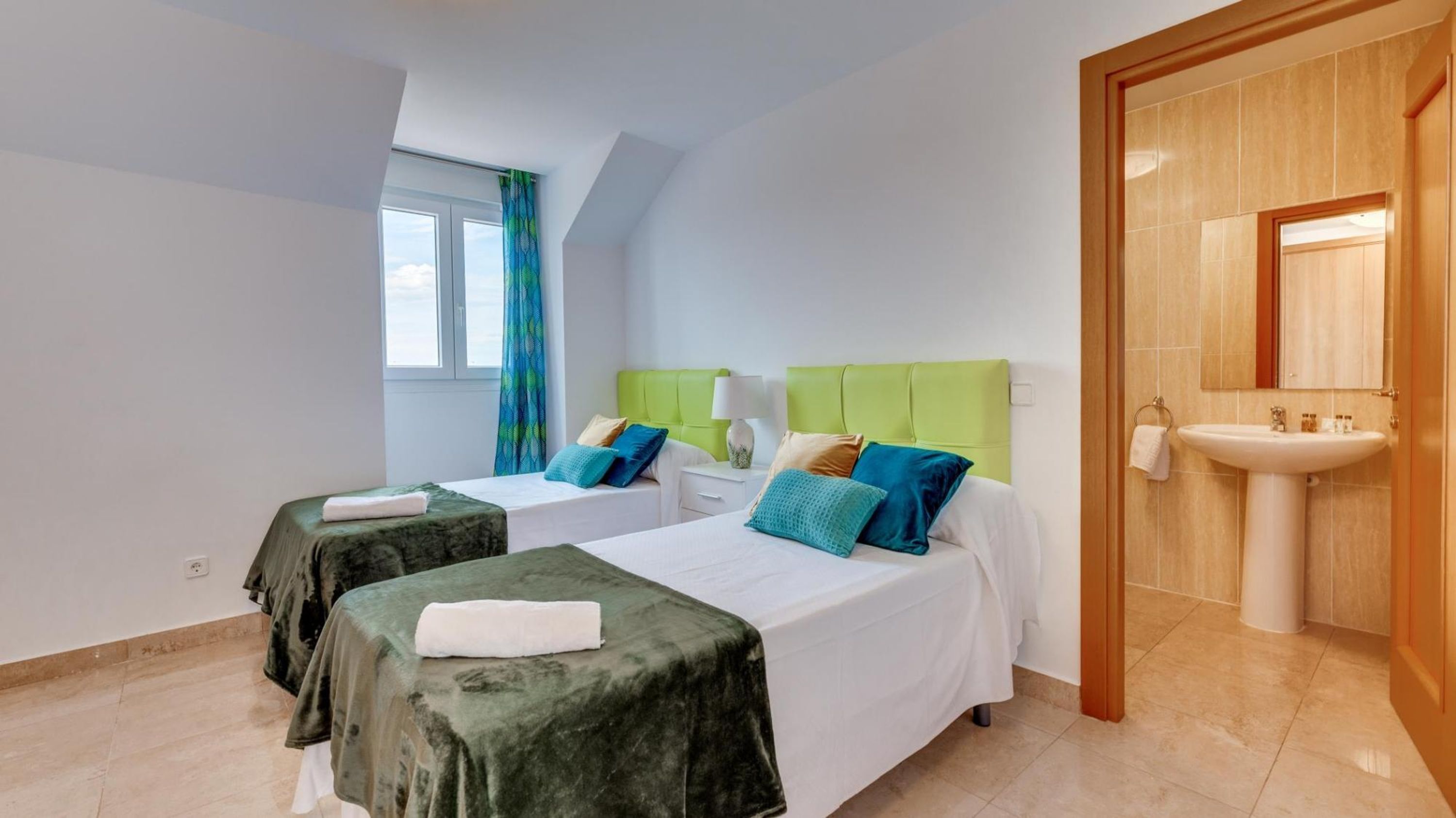 A hotel room with two beds, a bathroom with a sink, and a window with curtains.