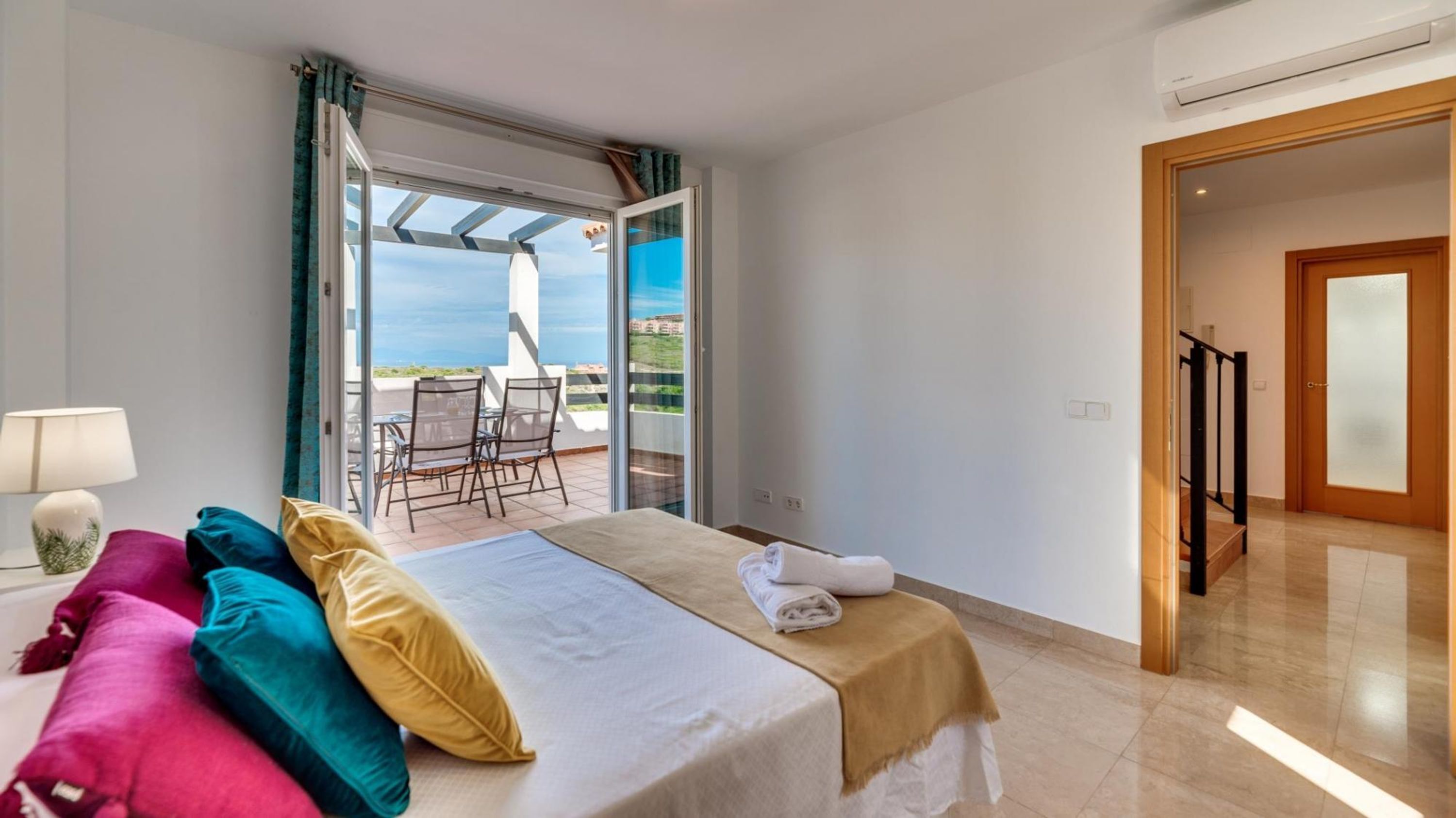 A hotel room with a bed, a chair, a table, and a view of the sea through a glass door.