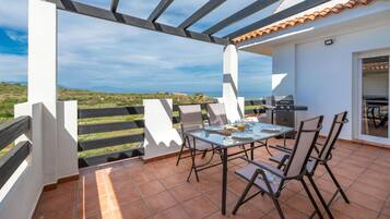 An outdoor patio with a table and chairs, a grill, and a view of the landscape.