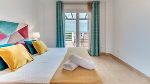 A hotel room with a bed, a bedside table with a lamp, a view of the outdoors through a glass door, and a balcony with chairs. - Hidden Treasure on a Virgin Paradise (Manilva)