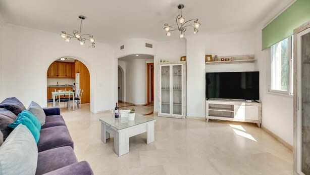 A modern living room with a sofa, coffee table, TV, and a kitchen visible through an archway. - Chic Urban Oasis in Estepona (Estepona)