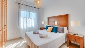 A hotel room with a large bed, two bedside tables, a wooden headboard, and a window with sheer curtains. - Chic Urban Oasis in Estepona (Estepona)
