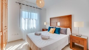 Ein Hotelzimmer mit einem großen Bett, zwei Nachttischen, einem Holzkopfende und einem Fenster mit durchsichtigen Vorhängen.