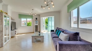 Ein geräumiges Wohnzimmer mit großem Fenster, einer Couch, einem Couchtisch und einem Fernseher.