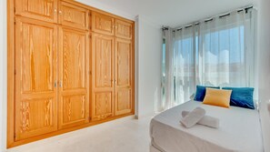 Ein Schlafzimmer mit großem Kleiderschrank, einem Bett mit Kissen und einem Fenster mit durchsichtigen Vorhängen.