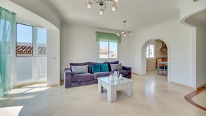 A spacious living room with a sofa, coffee table, and a view of the city through large windows. - Chic Urban Oasis in Estepona (Estepona)