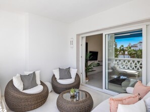 A balcony with wicker furniture, a glass door leading outside, and a small table with a plant. - Dos Dormitorios en Las Gaviotas (Marbella)