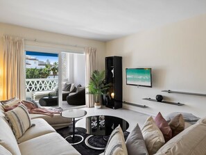 A modern living room with a sofa, coffee table, and a flat-screen TV mounted on the wall. - Dos Dormitorios en Las Gaviotas (Marbella)