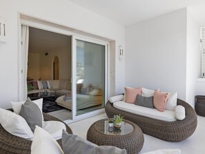 A modern living area with a sofa, two round wicker coffee tables, and a sliding glass door leading to an adjacent room. - Dos Dormitorios en Las Gaviotas (Marbella)